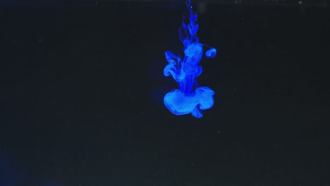 Slow-motion-video-of-blue-watercolor-ink-mixing-in-water-against-black-background