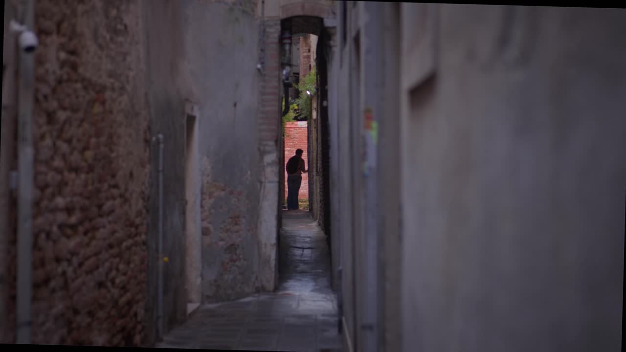 Silhouetted figure backlit in old narrow street alleyway, Venice