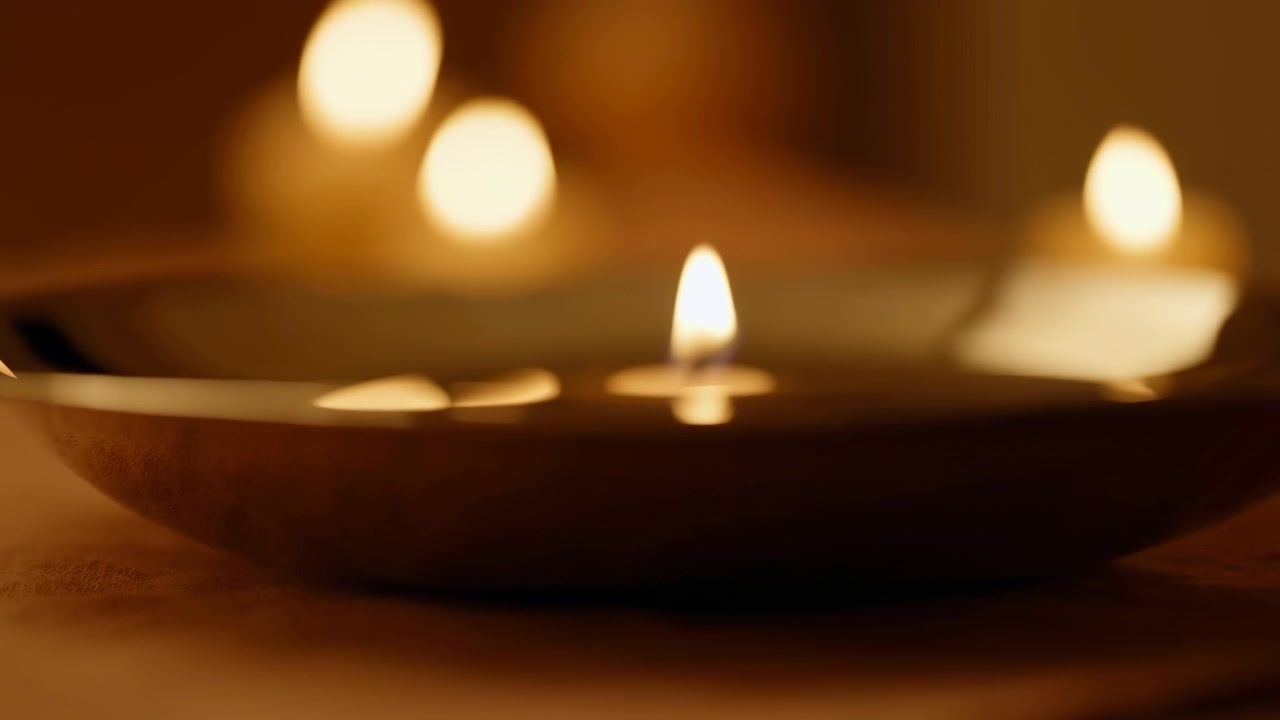 Sequenza iniziale di un portacandele scuro e poco profondo in primo piano in basso, mentre fiamme soffuse e brillanti sfocano sullo sfondo.