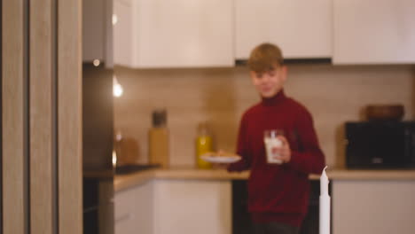 Camera-Focuses-On-A-Boy-Placing-A-Milk-Glass-And-A-Plate-Full-Of-Cookies-On-An-Empty-Table-With-Two-Candles,-Then-He-Leaves-The-Room