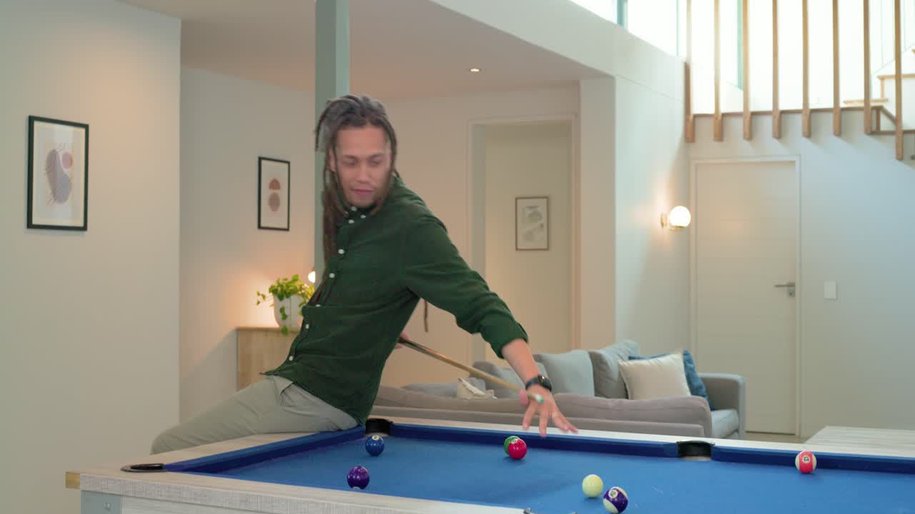 After striking ball on blue-felt pool table, man at home pumping stick realigning for next shot
