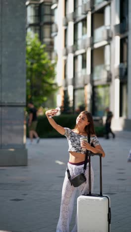 young woman taking a selfie in the city while traveling with a suitcase and coffee