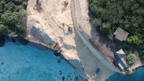top down drone video of turquoise waves crashing against environmental destruction of the limestone cliffs near pura luhur uluwatu temple, bali indonesia with massive earth clearing