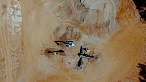 aerial top down shot of working excavator digging sand at sand quarry during sunny day - orbit shot