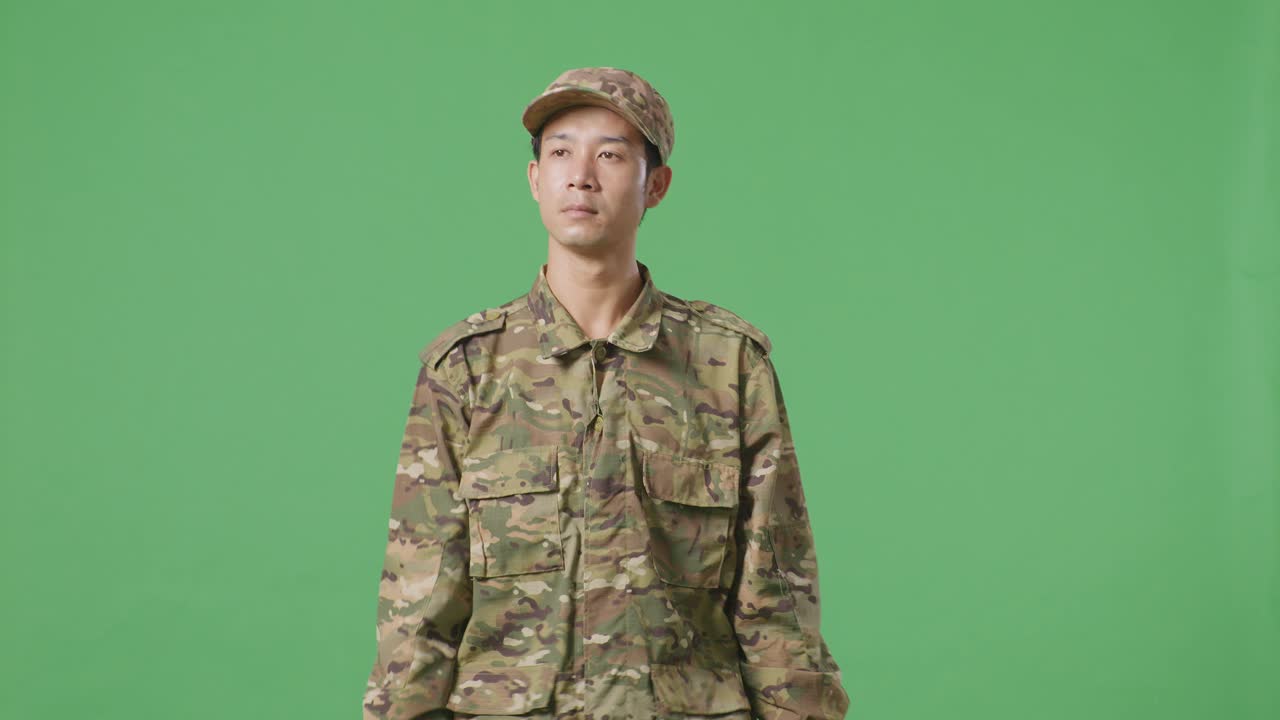 동양인 군인이 녹색 스크린 배경 스튜디오에서 걸어다니며 둘러보고 있습니다.