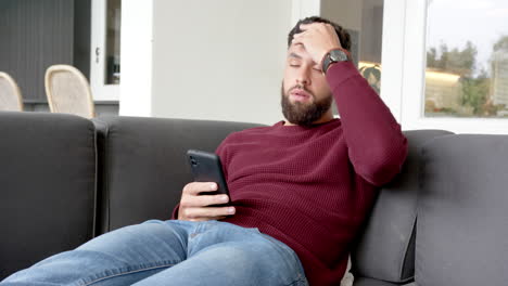 relaxing on couch, man using smartphone and looking stressed at home