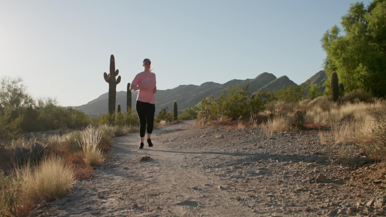 mujer millennial en forma corriendo por el camino del desierto con cactus mientras el sol se pone