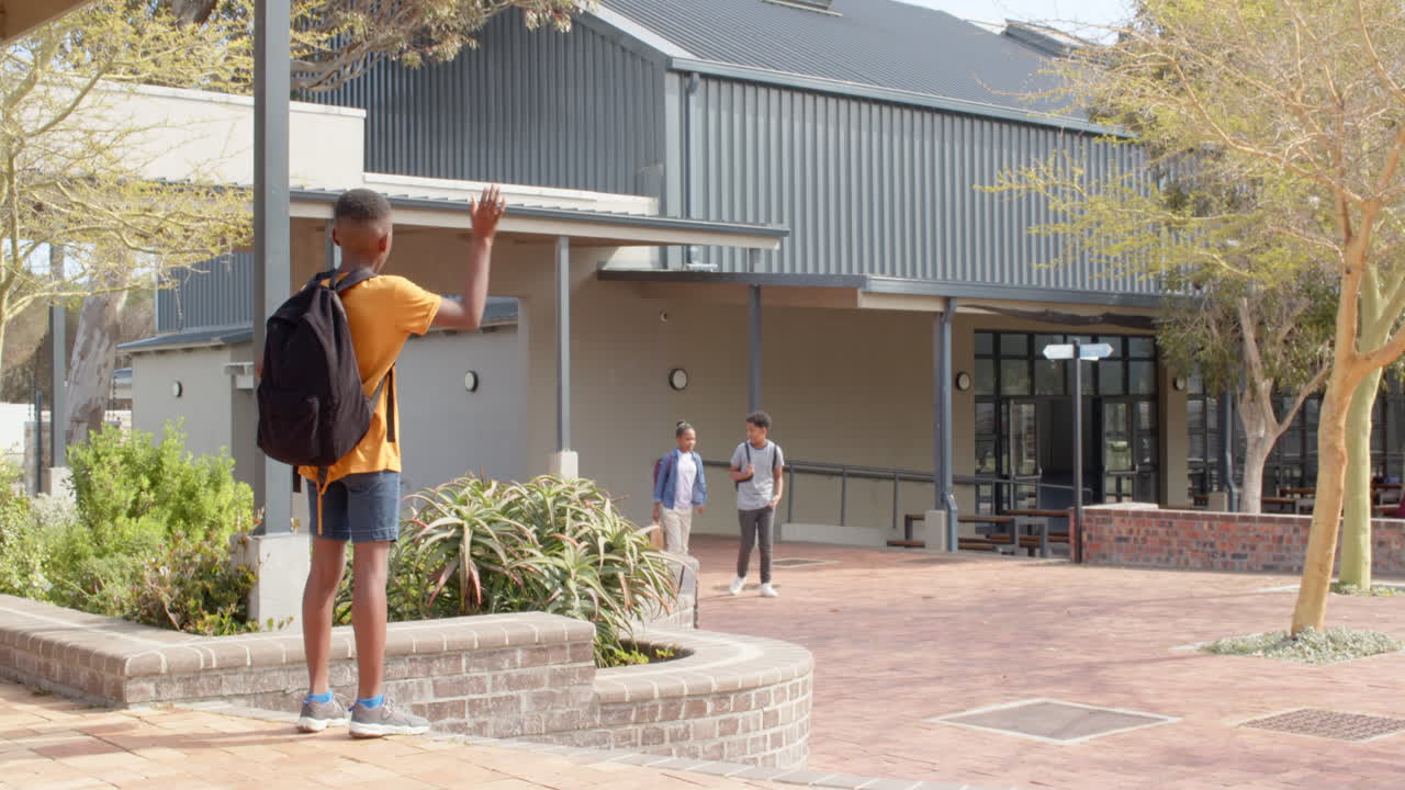 multiracial students greeting each other outside school, smiling and waving
