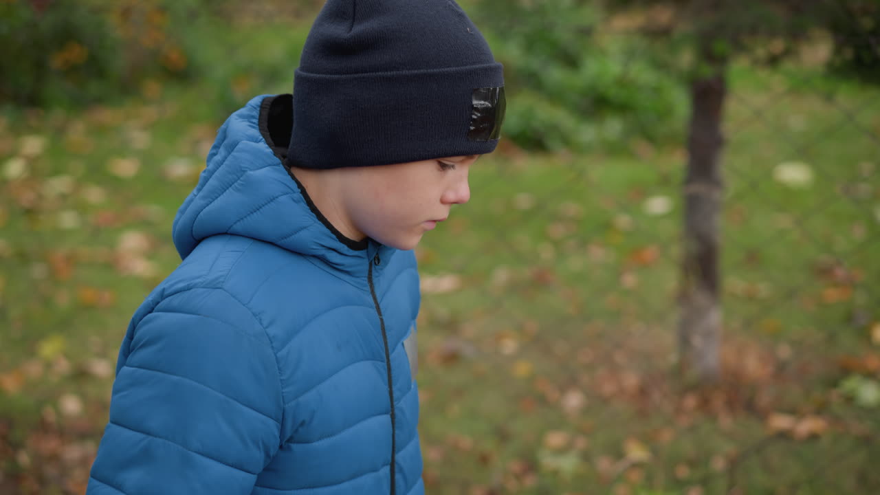 파란색 재과 검은색 모자를 입은 아이의 클로즈업은 어진 가을 잎을 특징으로하는 흐릿한 잔디 바탕으로 사려 깊게 내려다보고 있습니다.