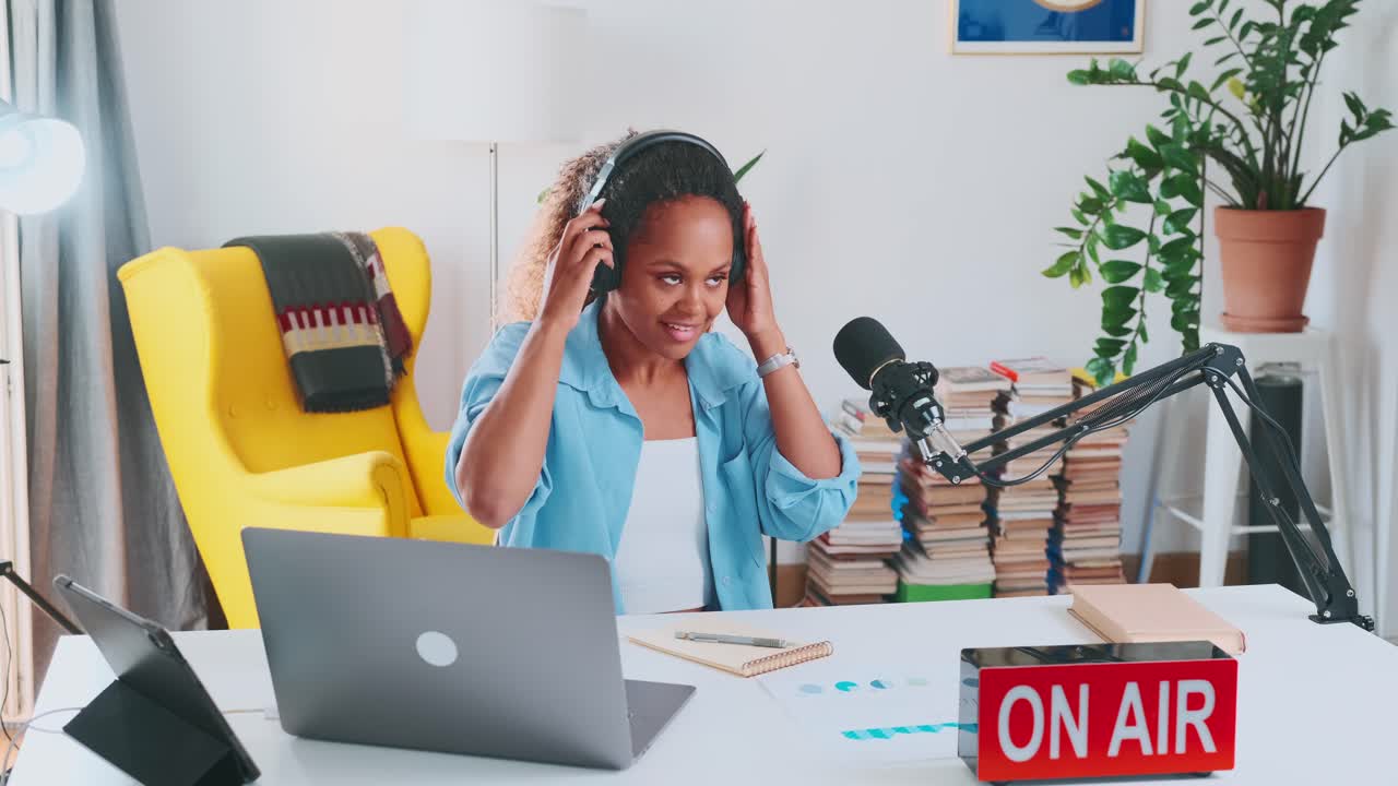 Ung afrikansk-amerikansk kvinde tager hovedtelefoner på og starter en live podcast.