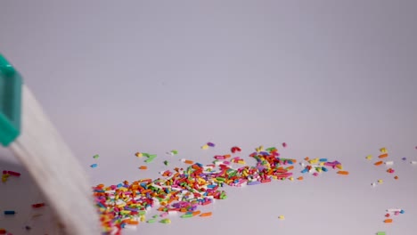 a hand uses a brush to sweep vibrant sprinkles on a white surface, creating dynamic patterns