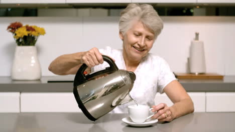 elderly woman pouring boiling water from kettle into cup