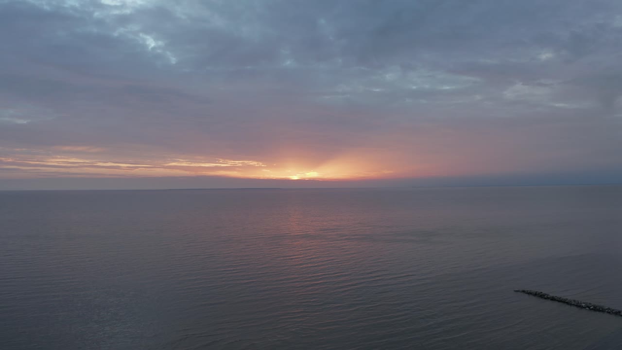 toma de drones de un mar tranquilo durante la puesta de sol con nubes coloridas alejándose revelando el bosque y la costa en 4k
