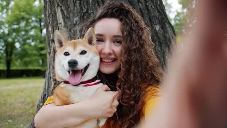 portrait of attractive lady taking selfie with puppy in park kissing hugging dog