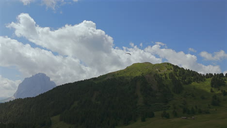 a paraglider floats over a lush green mountain landscape under a vast blue sky with fluffy clouds, capturing the essence of freedom and adventure