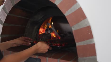 Mixed-race-female-chef-putting-a-plate-with-tomatoes-into-oven