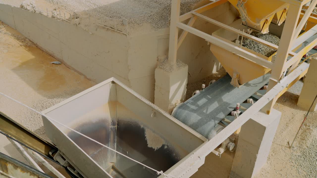 Large metal hopper, aggregate piles, and conveyor belts in action at a construction site in Karachi, highlighting industrial materials handling and cement batching operations