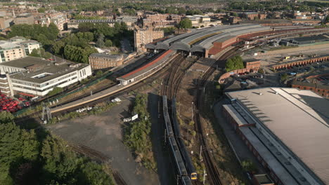 Schwenkende-Luftdrohnenaufnahme-Des-Bahnhofs-Von-York-Mit-2-Zügen,-Die-Den-Bahnhof-Verlassen-Und-Betreten,-Mit-National-Railway-Museum-Und-River-Ouse-Im-Blick---North-Yorkshire-United-Kingdom