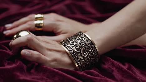 close-up of ornate gold cuff bracelet on hands resting on red velvet