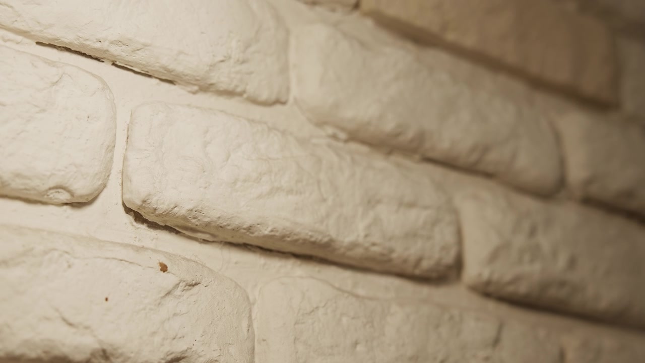 Close up of white brick wall with soft lighting highlighting texture details and subtle shadows. scene shows consistent close up view focusing on rough surface mortar lines color variations