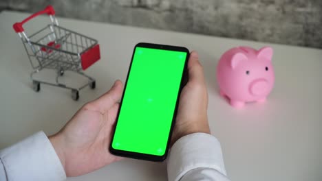 teléfono con una pantalla chromakey en las manos de un primer plano. vista superior de la caja de ahorros del teléfono inteligente y el carrito de compras copia el espacio sobre fondo blanco