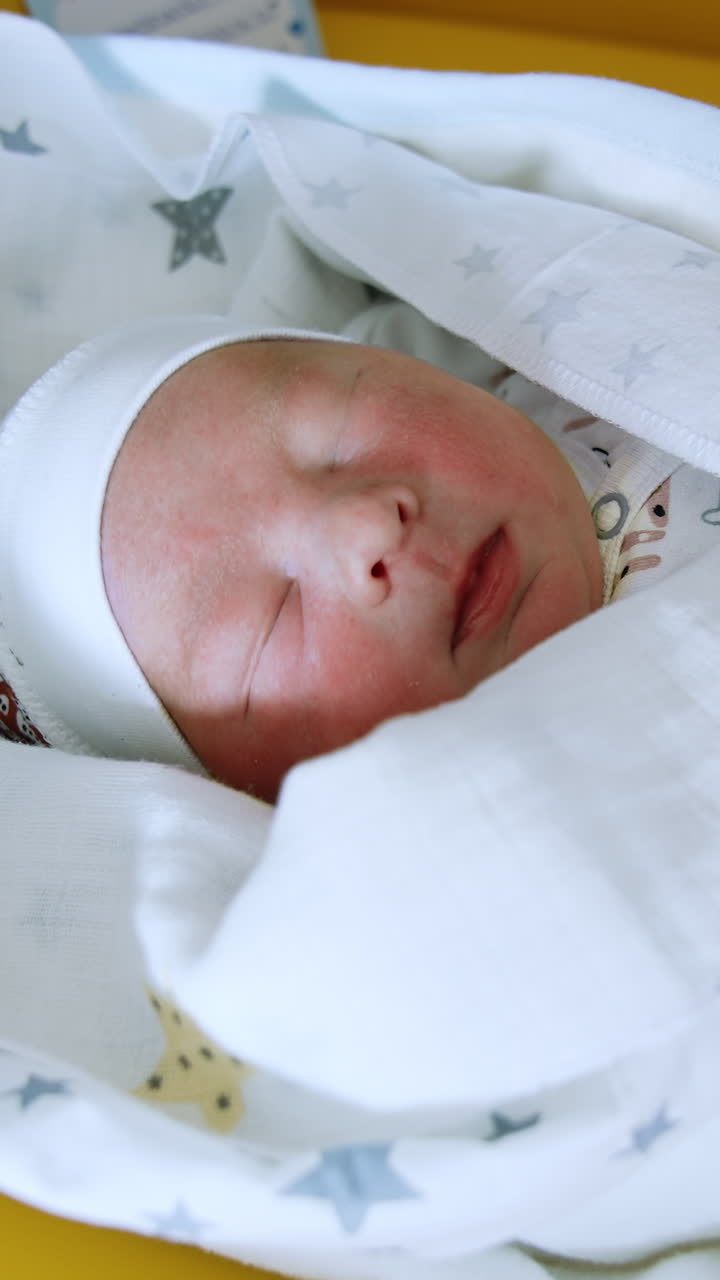 Newborn baby wearing cute cap sleeps peacefully covered in blanket. Close up. Top view. Vertical video