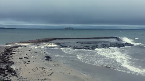 Mar-Agitado-Que-Golpea-Una-Poza-De-Marea-En-Salthill,-Con-La-Bahía-De-Galway-Y-Un-Barco-De-Crucero-Al-Fondo