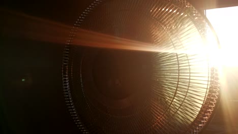 4k footage of indoor fan during sunset. sun breaking through propellers and guarding grid. lens flares being caused by low sun just above the horizon behind the ventilator.