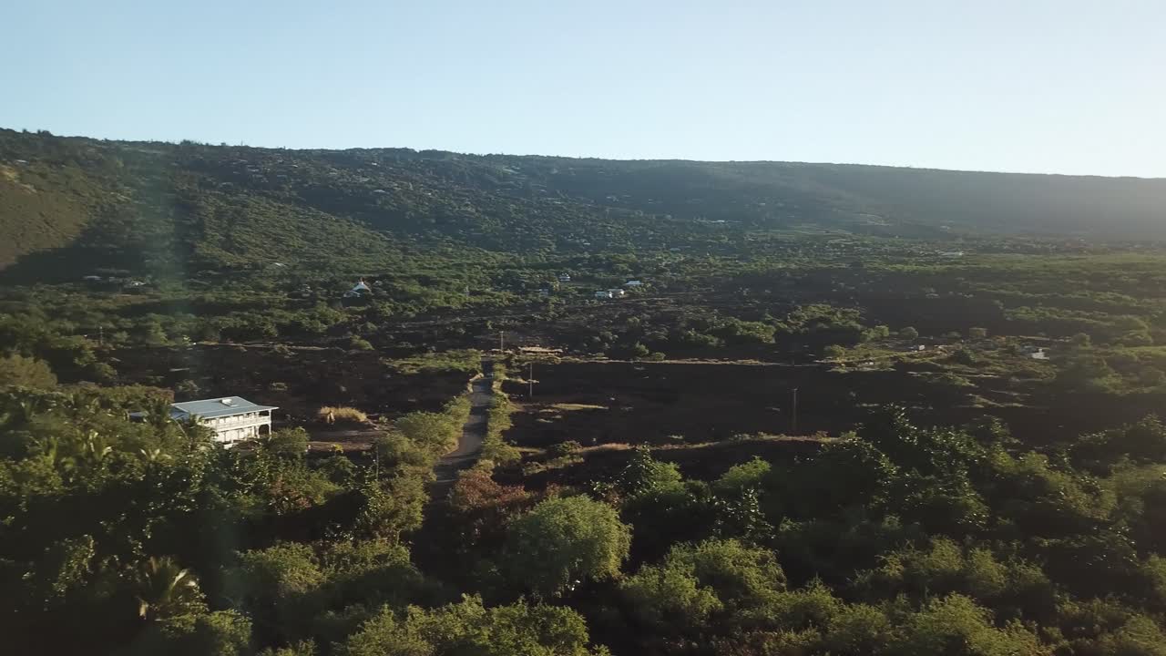 Golden sunlight illuminates a wide green landscape as it rises over the distant ridge. Captured from above, this tranquil scene highlights natural light, open terrain, and early morning atmosphere.