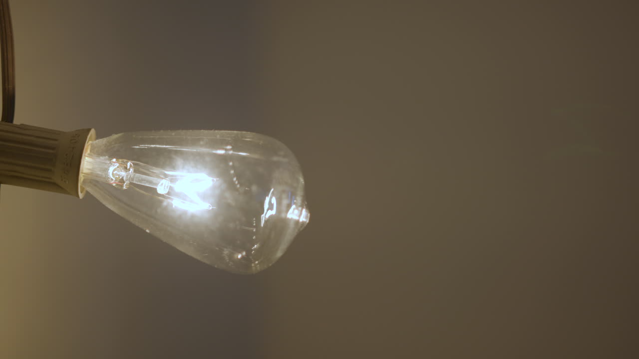 paneo lento a una bombilla en un hilo que se enciende y se apaga con una subida de tensión