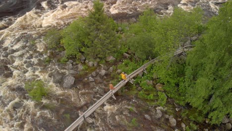 aerial footage by drone of two men walking over small bridge over kalix rapid