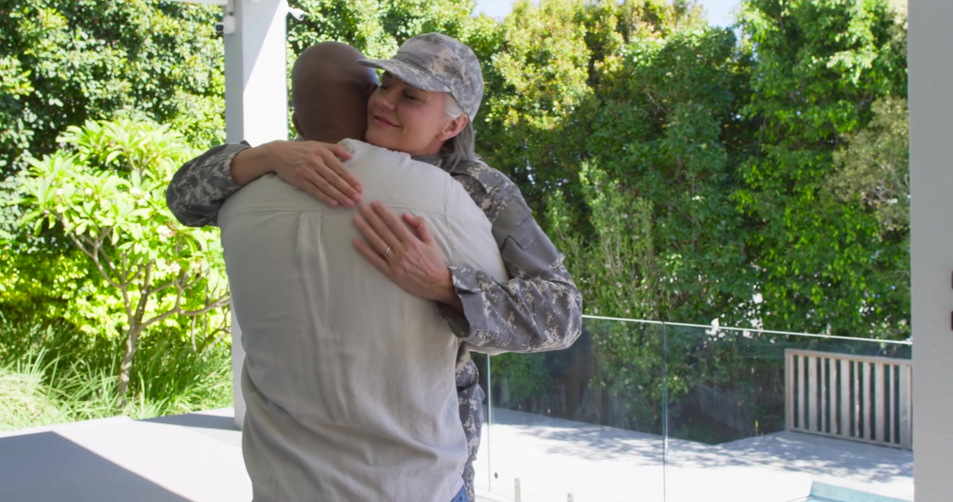 Coppia che si ricongiunge sul portico, donna militare in mimetica che abbraccia un uomo afroamericano