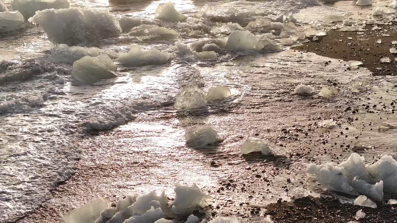 waves push glacial ice onto the glowing pebbled shore of Diamond Beach