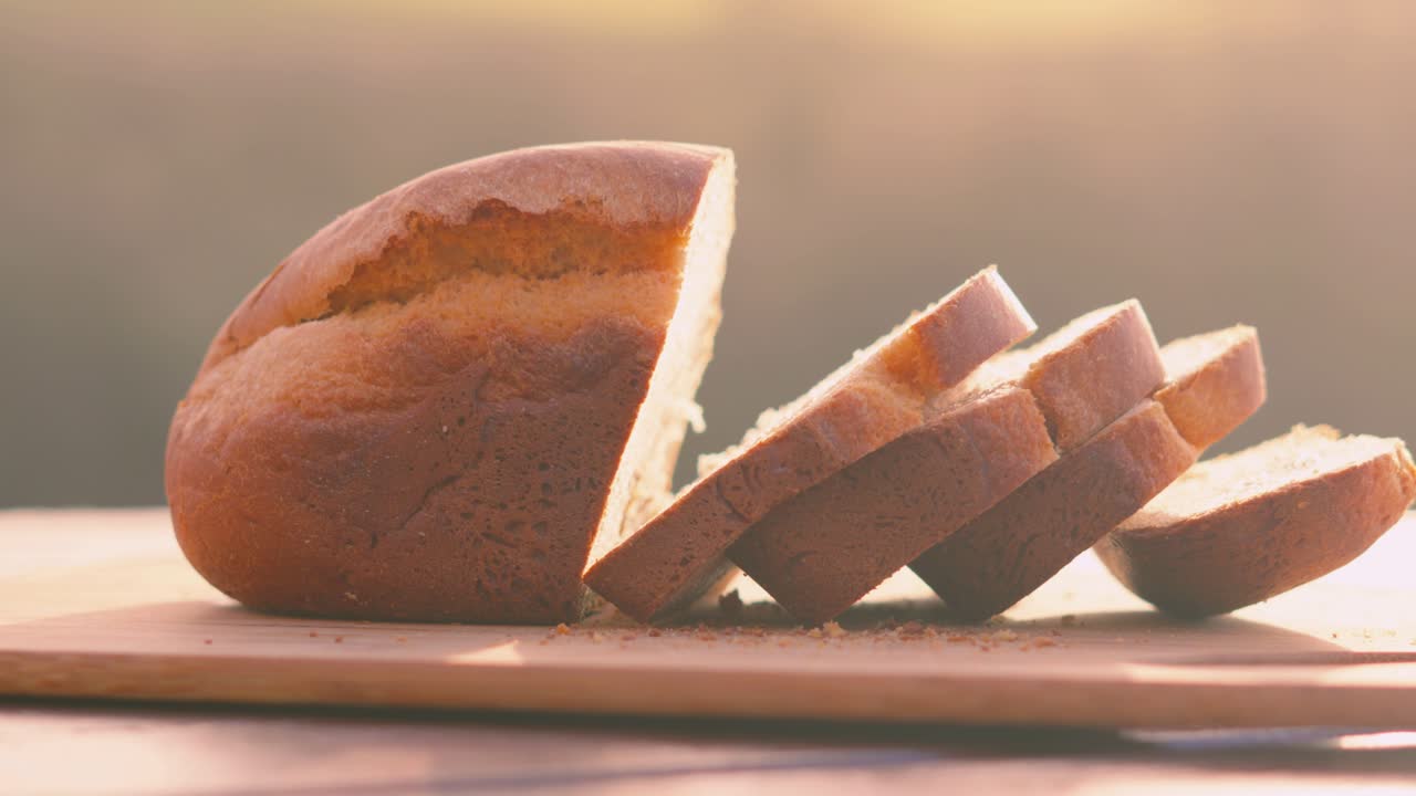 Outdoors Morning Sunlight on Freshly Baked Homemade White Bread Loaf with Slices on Wooden Chopping Board with Fields Background. Home Baking Footage with Simple Healthy Ingredients 4K.