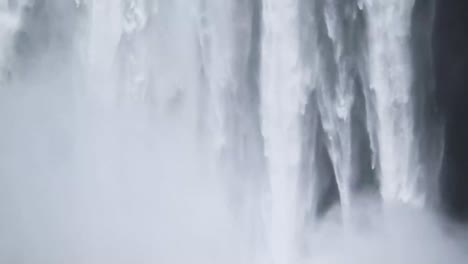 man in red sweater stading at the bottom of the skogafoss waterfalll in iceland
