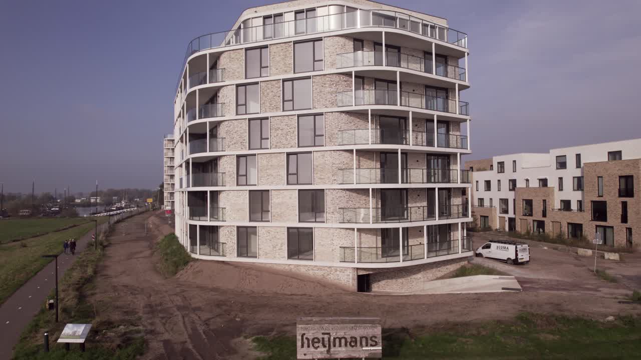Close up sign of Heijmans engineering backwards aerial movement revealing rising exterior facades of newly build luxury apartment towers Pracht along riverside of river IJssel