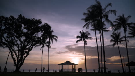 tanjung aru beach - silhouetted tropical palms and people tourists walking against dramatic sunset sky by the sea at shangri-la resort kota kinabalu, sabah, malaysia - static wide angle