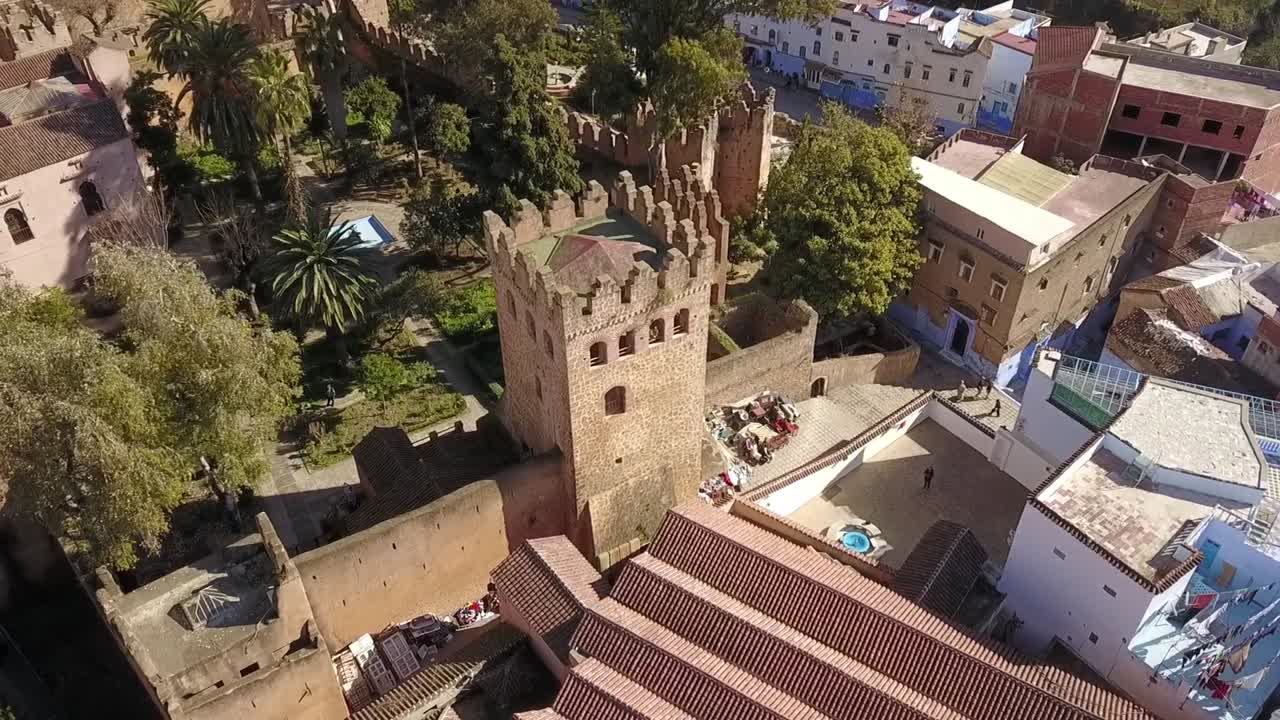 Zachwycający widok lotniczy HD na historyczną wieżę Kasbah i ogrody w Chefchaouen. Przedstawia starożytną kamienną fortecę i tradycyjną architekturę Marokańskiego Błękitnego Miasta. Idealny do podróży i historii.