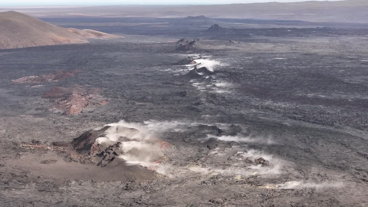 Aerial view of Icelandic volcanic terrain with multiple steam vents and blackened lava fields stretching across the landscape