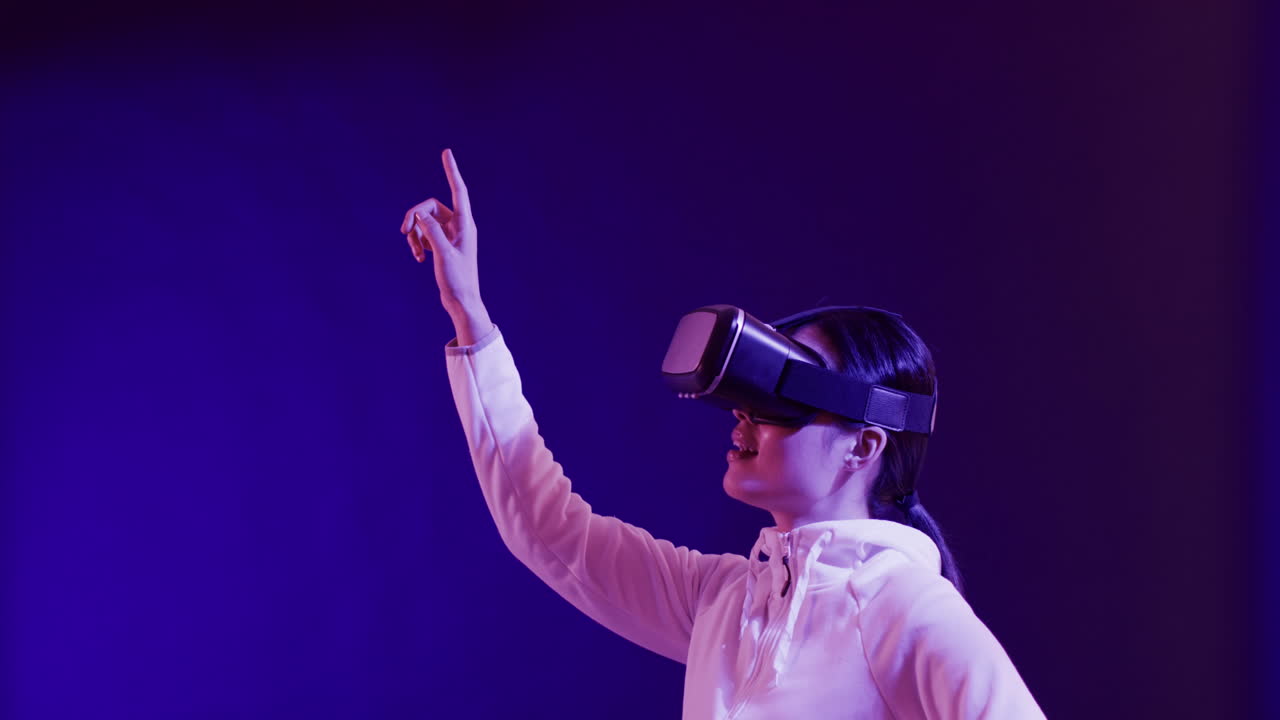 Asian woman using vr headset, touching virtual screen on blue background, copy space, slow motion