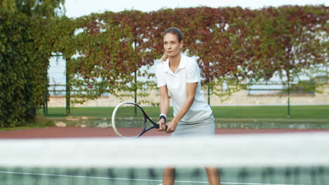 スポーツコートで晴れた夏の日にテニスをし、ラケットでボールを打つ金髪の女性