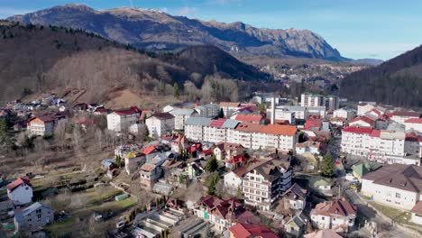 Drone-backwards-shot-of-ancient-city-named-Sinaia-with-mountain-range-panorama-in-background---Sunny-day-in-Romania---Ascending-flight