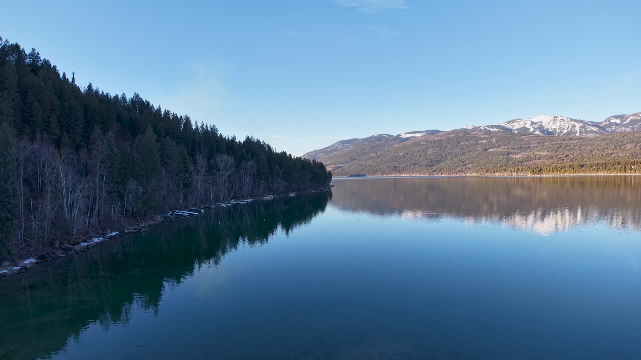 Whitefish, Montana yakınlarında çam ormanlarını ve uzaktaki dağları yansıtan sakin bir dağ gölünün hava görüntüsü.
