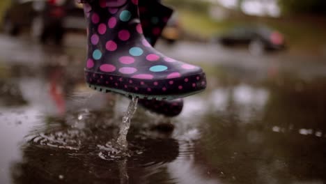 unrecognizable girl jumping in a pool of water during rainy day with waterproof boots, close up of the feet with selective focus