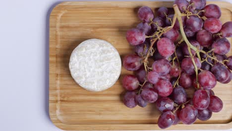 camembert cheese and red grapes on a wooden board