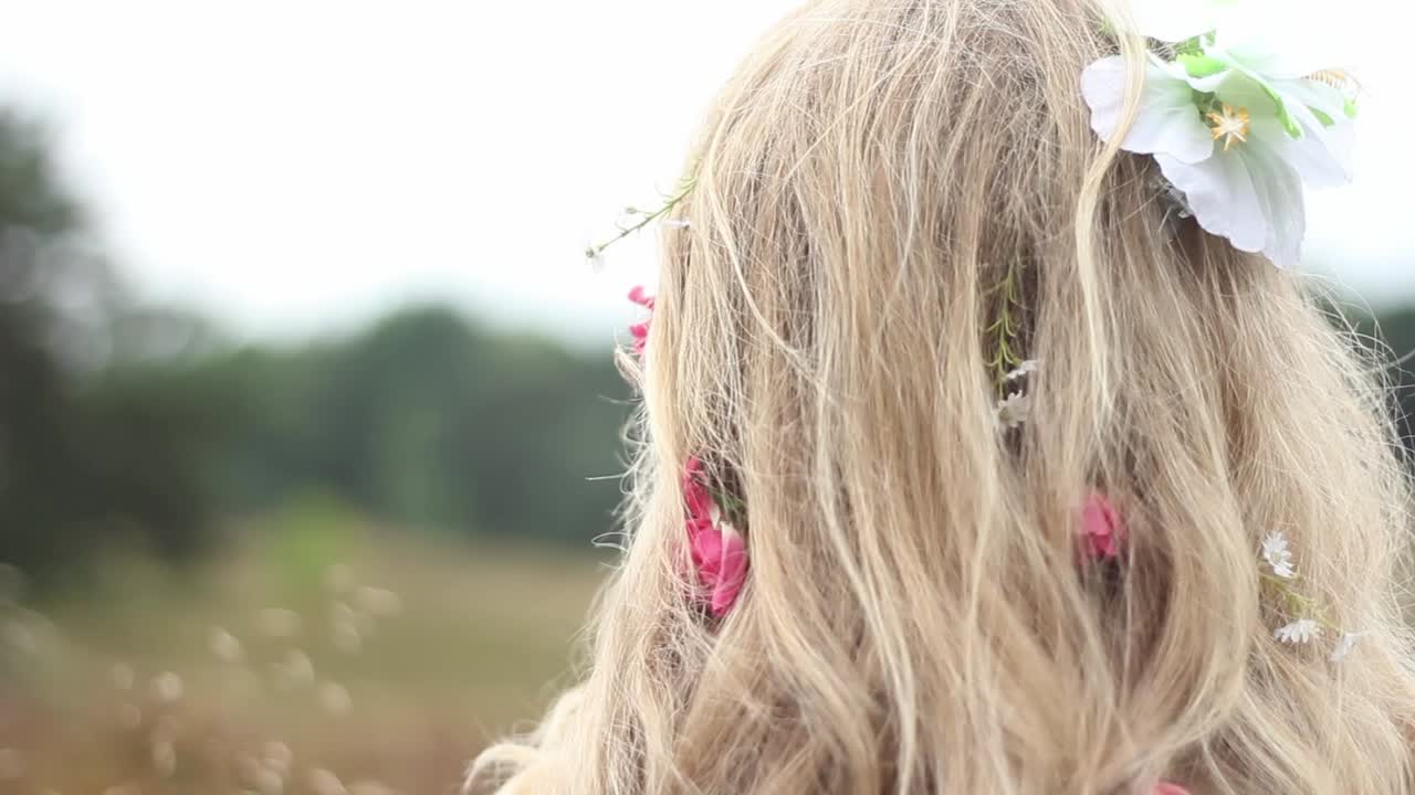 panorámica desde una pequeña planta de trigo hasta el largo cabello rubio de una mujer con flores trenzadas