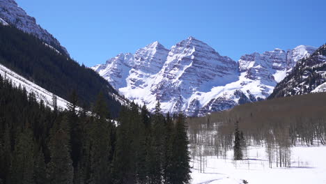 mid winter maroon bells aspen wilderness colorado bluebird early morning fresh snow cinematic pan left from snowmobile trail