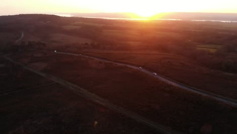 disparo aéreo hacia adelante sobre woodbury common en devon, inglaterra y una calle muy transitada con el sol poniéndose