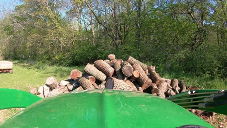POV while operating a green tractor with hydraulic forks to move cut logs