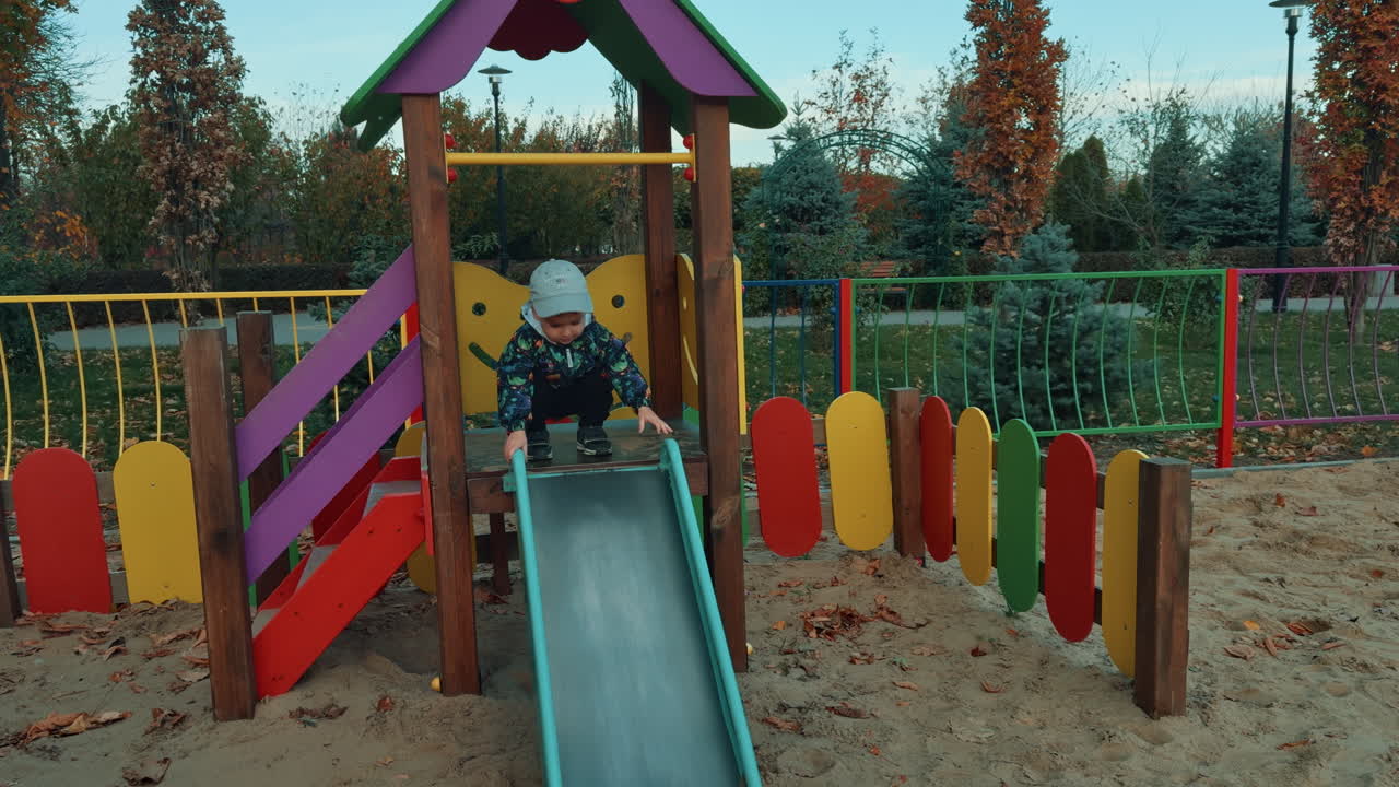 Energetic Caucasian toddler is on the playground. Happy cheerful kid is on the slide in autumn.